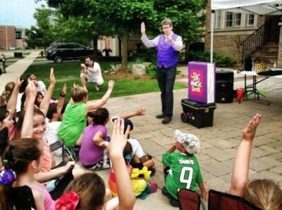 Robert performing outdoors as children in the audience raise their hands