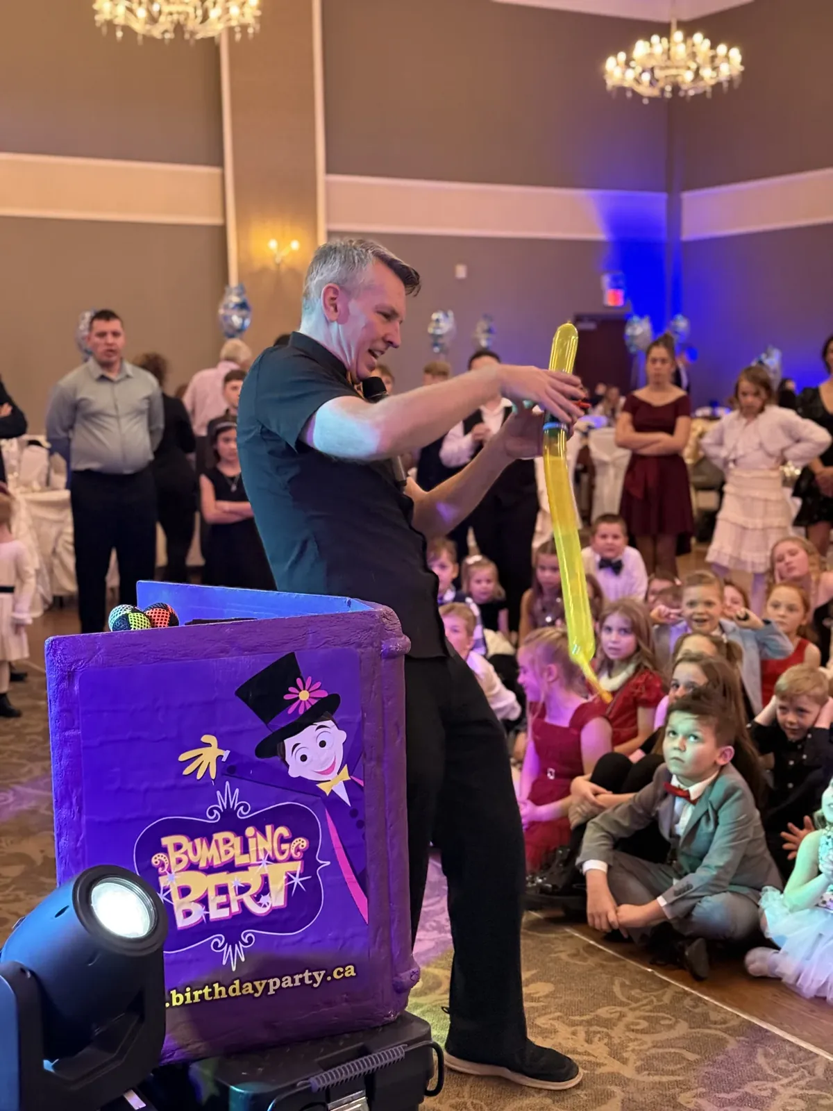 Robert Presswood performing as Bumbling Bert with a yellow balloon while children watch